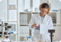 scientist stood in a lab wearing a white coat examining data on a clip board